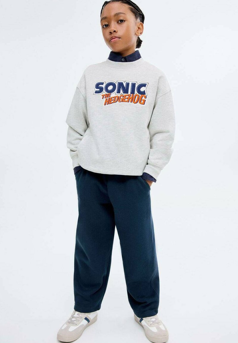 Šedá mikina s grafikou "SONIC THE HEDGEHOG", námornícke nohavice a biele tenisky s modrými akcentmi. Uvoľnen�ý strih a rebrované manžety.
