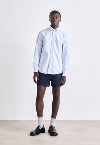 Lichtblauw overhemd met knopen, marineblauwe shorts, grijze sokken en zwarte instappers; minimalistisch ontwerp, gladde textuur, op maat gemaakt.