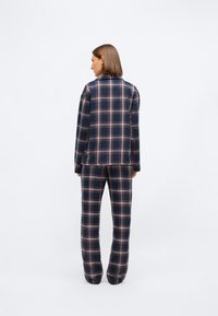 Setti loungewear verkkopaidasta tummansinisenä, vihreänä ja punaisena. Pitkähihaisessa paidassa on kaulus; housuissa on joustava vyötärö. Pehmeä kangastuntuma.