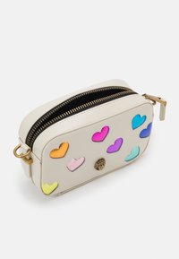 Krémová kožená taška se zipovým uzávěrem a zlatými kovovými detaily, zdobená barevnými srdíčkovými aplikacemi v růžové, oranžové, fialové a modré barvě.