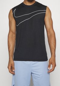 Débardeur de sport noir sans manches avec un col arrondi, arborant un logo Nike argenté en forme de swoosh sur la poitrine et une texture de tissu lisse.