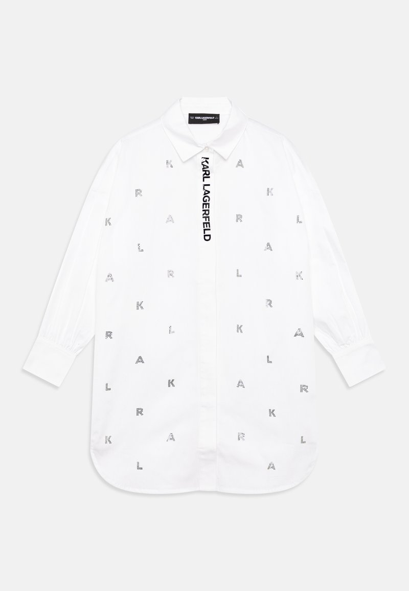 Balta pogu krekls ar garām piedurknēm, kas rotāts ar izkaisītām sudraba burtiņu akcentiem un vertikālu logo birku priekšpusē. Gluda kokvilnas auduma.