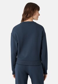 Námořnická modrá mikina s žebrovanými manžetami a spodním lemem, která má uvolněný střih a viditelné švy. Měkká tkanina a design s kulatým výstřihem.