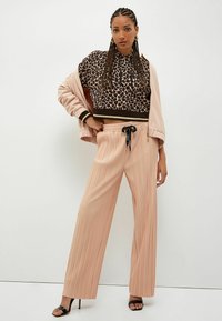 Felpa cropped con stampa giraffa marrone e nera, con un accento dorato, abbinata a pantaloni ampi plissettati rosa chiaro e sandali neri con tacco.