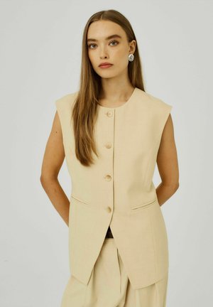Beige mouwloze vest met een rechte snit, voorzien van vier knopen en twee zijzakken, gemaakt van soepele stof, gecombineerd met bijpassende broek.