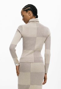 Beżowy i jasnoszary golf z pionowymi paskami, o prążkowanej fakturze, dopasowanym kroju, z długimi rękawami i wysokim kołnierzem.