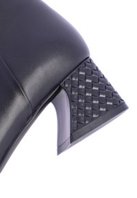 Zapato de tacón alto negro con parte superior de cuero liso y acentuación de tacón de bloque con textura trenzada. Presenta una silueta elegante y un acabado brillante.