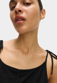 Top in tessuto nero con spalline sottili legate alle estremità, scollatura arrotondata e finitura liscia e texture.
