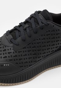 Svart sneaker med en texturerad ovandel med rutmönster, hållbara syntetmaterial och en tjock gummisåle. Snörningen är i matchande färg.