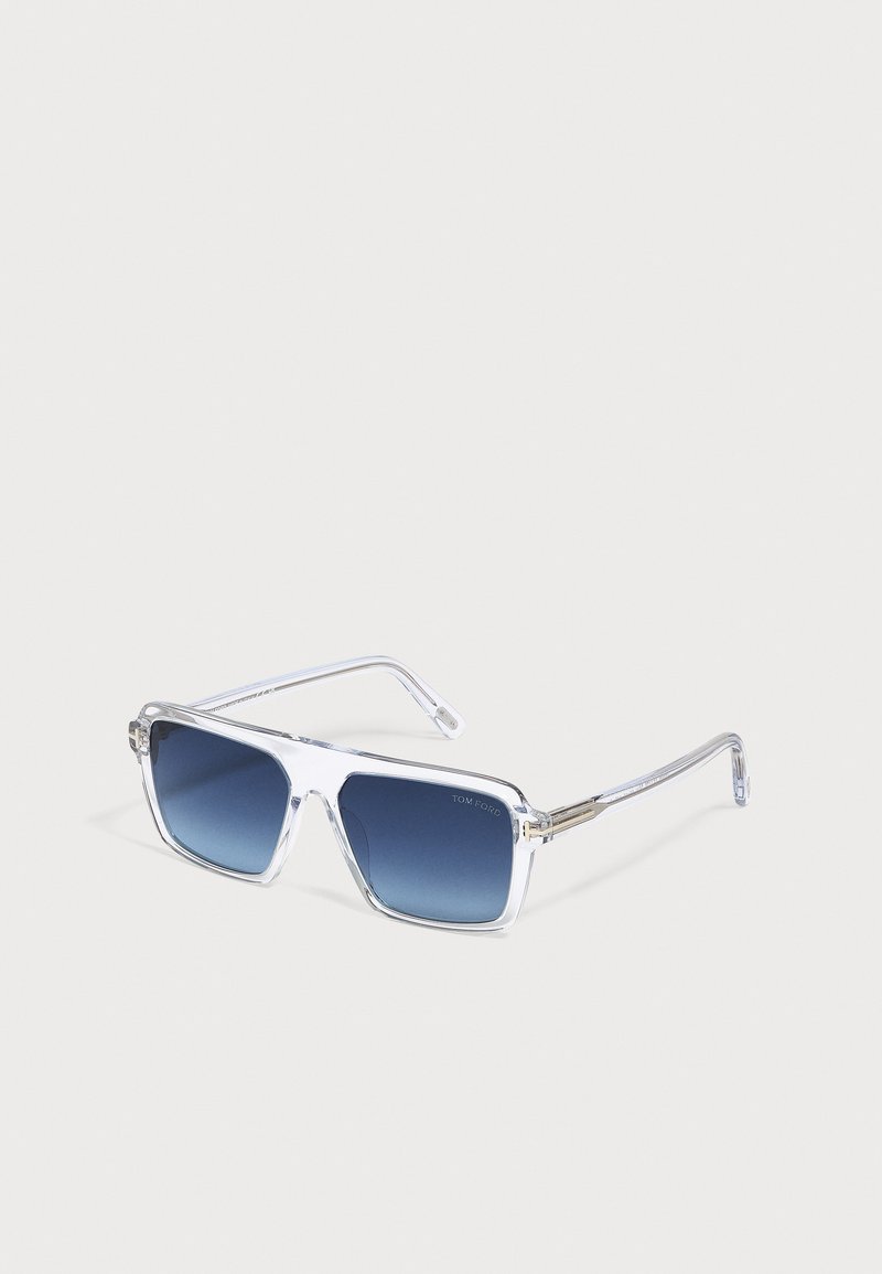 Lunettes de soleil rectangulaires transparentes avec verres à dégradé bleu posées sur une surface blanche.
