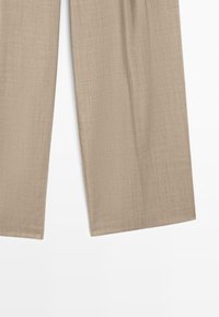 Pantalons larges beige en tissu texturé, avec une finition lisse et une coupe ajustée, sans poches visibles ni embellissements.