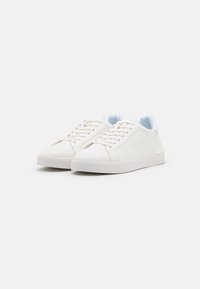 Zapatillas blancas con un acabado de cuero suave, diseño de cordones, cuello acolchado y suela de goma texturizada, presentando una estética minimalista.