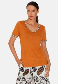 Oranje t-shirt met korte mouwen en een diepe v-hals, met een zwart-witte decoratieve rand op de halslijn en mouwen. Zachte textuur.
