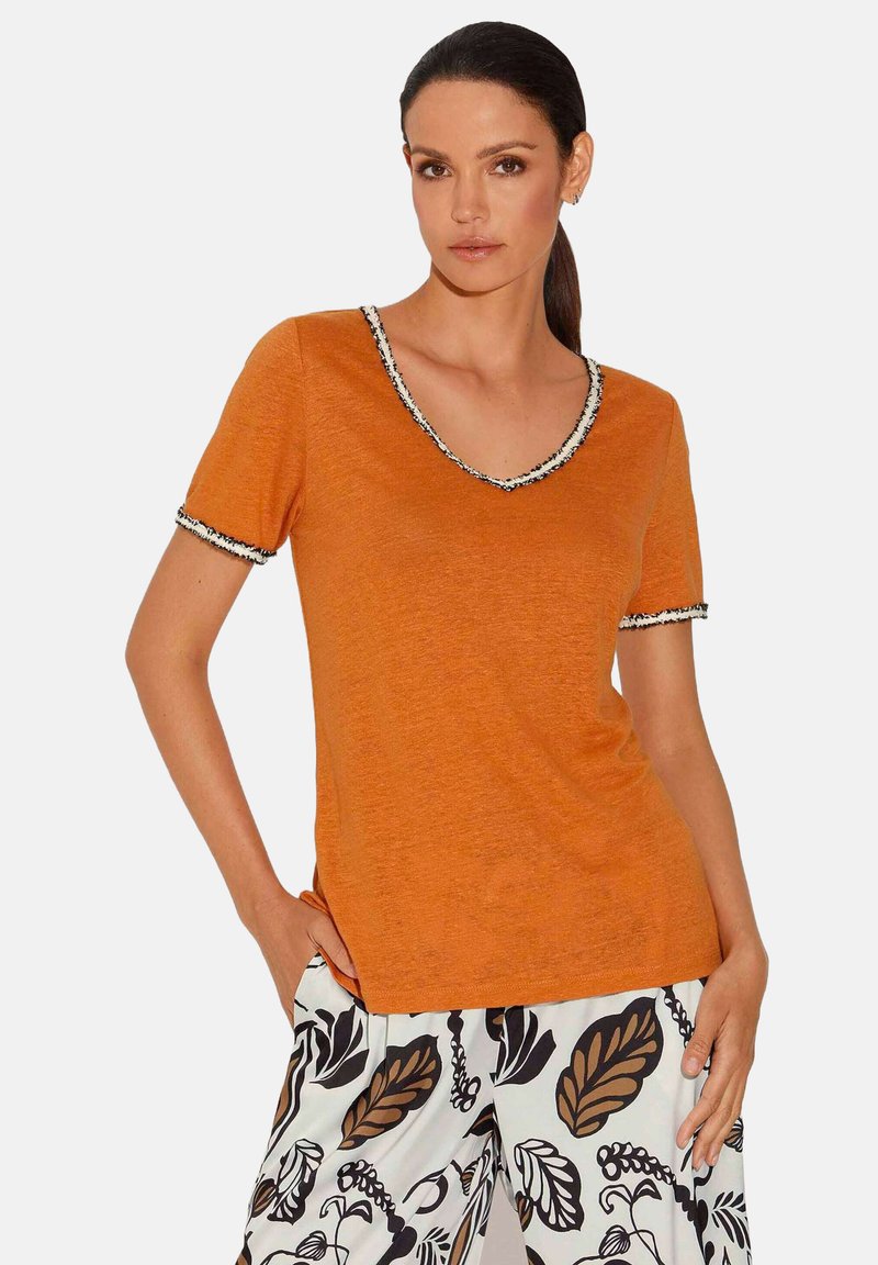 Oranje t-shirt met korte mouwen en een diepe v-hals, met een zwart-witte decoratieve rand op de halslijn en mouwen. Zachte textuur.