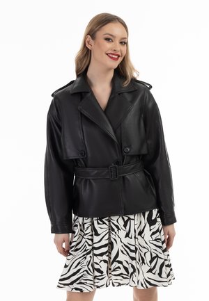 Zwarte leren jas met een tailleband, oversized revers en knopenaccenten, gedragen over een geplooide rok met zebra-print.