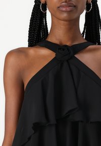 Rochie halter neagră, cu detaliu floral răsucit la guler și design cu volane stratificate. Țesătură fină, cu un ușor luciu.