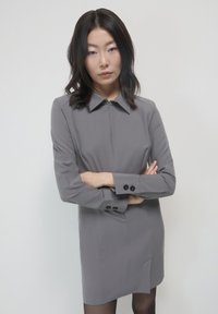 Abito grigio con colletto a punta, maniche lunghe, chiusura zip frontale e bottoni decorativi sui polsini. Tessuto liscio con una vestibilità sartoriale.