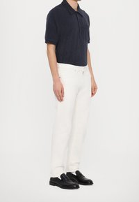 Polo de terry en color navy, jeans rectos blancos y mocasines negros. El polo tiene mangas cortas y un bolsillo en el pecho. Texturas suaves y lisas.