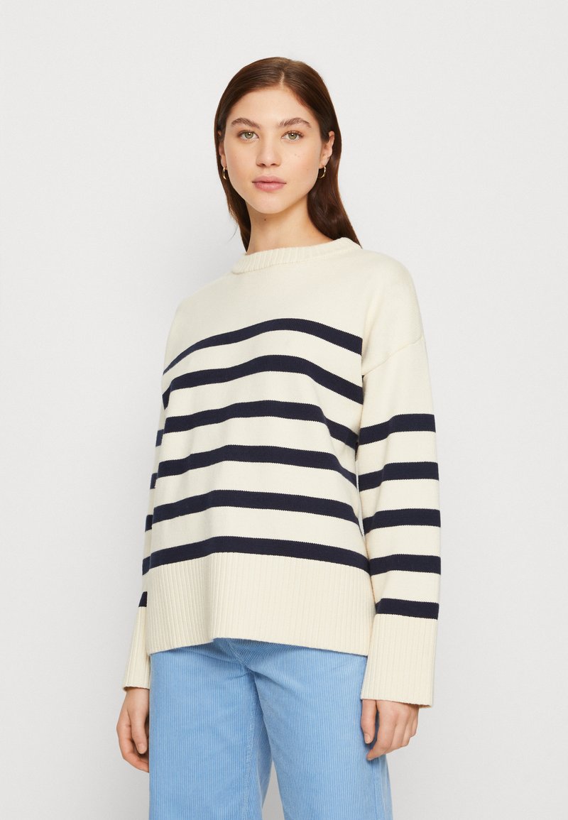 Cream sweater with dark navy horizontal stripes, ribbed hem and cuffs, relaxed fit, crew neckline, displayed on a model against a neutral background.