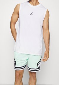 Hvid ærmeløs skjorte med en sort logo på brystet, kombineret med mintgrønne mesh-shorts med sorte og hvide accenter og striber.