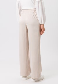 Pantalons larges de couleur beige clair en tissu lisse, dotés d'une taille élastique et d'une coupe décontractée. Assortis avec des chaussures blanches.