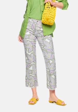 Woman wearing green shirt and patterned pants holding yellow woven bag, with matching yellow open-toe slide sandals.