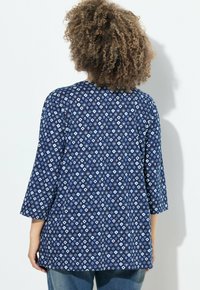 Tunic blu navy con motivi geometrici a diamante bianchi, maniche a tre quarti e vestibilità comoda. Tessuto morbido con una texture liscia.