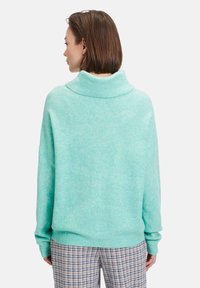 Licht muntgroene oversized trui met een hoge kraag, gestructureerd hexagonaal patroon en geribde mouwen, gecombineerd met broek met een geruit patroon.