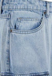 Lyseblå denimjeans med en slidt finish, der har en baglomme, kontrastsyninger og metalhardware på taljeelastikken.