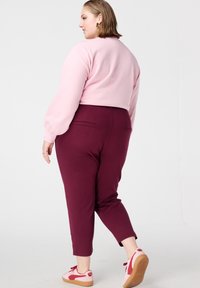 Sweat-shirt rose court, pantalon ajusté bordeaux et baskets rose/rouge, mettant en valeur un tissu doux, une coupe effilée et des détails subtils de poches arrière.