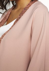 Vaaleanpunainen sifonkikimono, jossa on teksturoitu ja kiiltävä ruusukultatrimmaus. Kimonoissa on löysät hihat ja valuvasti laskeutuva siluetti.