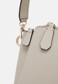 Lys grå tekstureret håndtaske med sorte accenter, har gyldent hardware og en aftagelig rem med en krog.