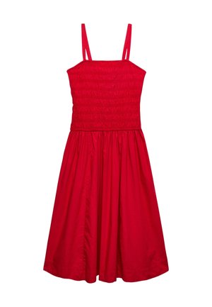 Kvinde iført rød ærmeløs midikjole, cremefarvet cropped jakke, rød vævet clutch og sorte sandaler med røde og hvide flettede stropper.