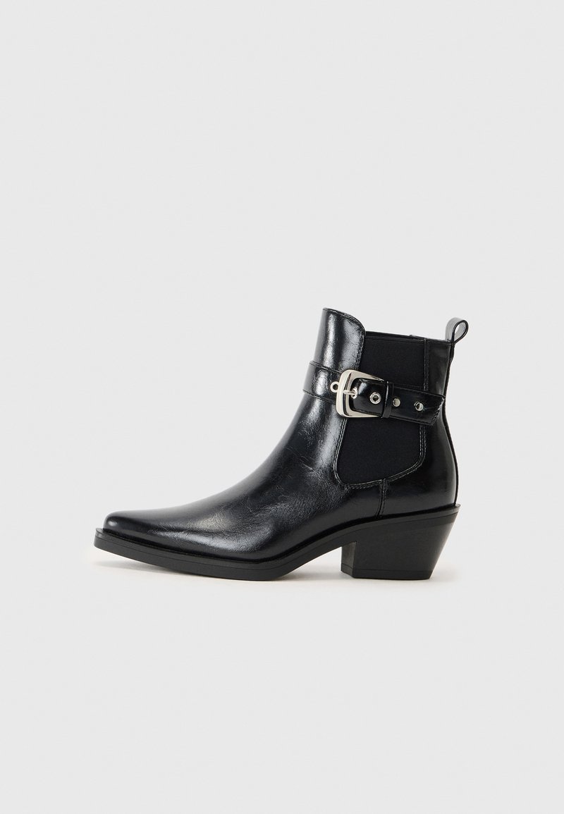 Bota de tornozelo em couro preto com bico pontudo, salto pequeno, painéis elásticos laterais e um detalhe de fivela decorativa. Acabamento liso.