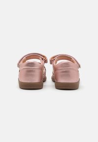 Rosa metalliske sko med lukket tå og teksturert overflate, justerbar stropp og brun såle, med sidedrag som gir ventilasjon.