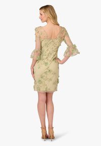 Abito corto e aderente in verde tenue. Maniche trasparenti e ricamate con accenti floreali. Design a V sulla schiena. Tacchi che completano l'outfit.