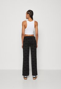 Zwarte wijde broek heeft een textuurontwerp met een herhalend patroon. Gecombineerd met een aansluitende witte crop top en sneakers.