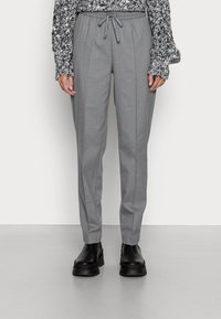 Grau maßgeschneiderte Hose mit einem Kordelzugbund, ausgestattet mit einem gefalteten Design. Kombiniert mit einem strukturierten schwarz-weißen Pullover und schwarzen Stiefeln.