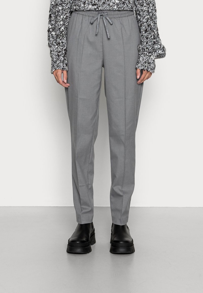 Grau maßgeschneiderte Hose mit einem Kordelzugbund, ausgestattet mit einem gefalteten Design. Kombiniert mit einem strukturierten schwarz-weißen Pullover und schwarzen Stiefeln.