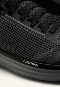 Czarny but sportowy z teksturowaną siateczkową cholewką, płaskimi sznurowadłami i oznaczeniem COREXFOAM na podeszwie środkowej. Lekko wygięta podeszwa dla wsparcia.