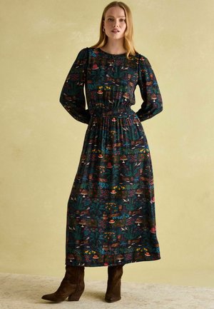 Long-sleeve maxi dress in dark fabric with colorful floral and fruit patterns. Bodice features gathered detail; paired with knee-high brown boots.