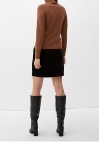 Brauner Rollkragensweater, schwarzer Cordrock und schwarze kniehohe Stiefel. Glatte Textur oben; der Rock hat Fronttaschen und einen geraden Schnitt.