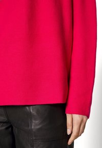 Pull en maille fuchsia à coupe décontractée, avec poignets et ourlet côtelés. Porté sur un pantalon en cuir noir lisse.