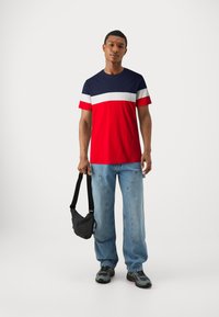 Rød, marineblå og hvid stribet crew-neck t-shirt lavet af bomuld. Båret med lyseblå denim jeans og en sort crossbody taske. Grå sneakers.