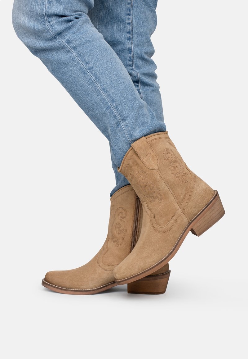 Botines de ante color beige con punta afilada, detalles de costura y tacón apilado. Combinados con jeans de mezclilla azul claro.