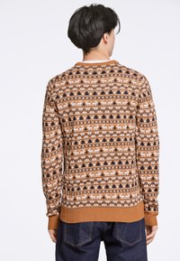 Braun gemusterter Pullover mit geometrischem Design, weißen Rehen und Bäumen, gerippten Bündchen und Rundhalsausschnitt. Weiches Strickmaterial.