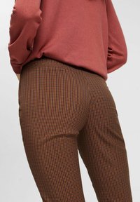 Brązowe spodnie w kratę o dopasowanym kroju i subtelnej fakturze. Połączone z bordowym swetrem, podkreślającym talię.