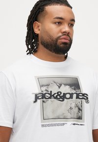Λευκό βαμβακερό t-shirt με μεγάλο ασπρόμαυρο γραφικό βουνό και το κείμενο «jack&jones». Λαιμόκο�ψη στρογγυλή, κοντά μανίκια, άνετη εφαρμογή.