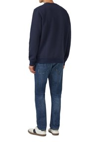 Granatowa teksturowana bluza z okrągłym dekoltem, w zestawieniu z jasnoniebieskimi dżinsami i białymi trampkami z czarnym paskiem.