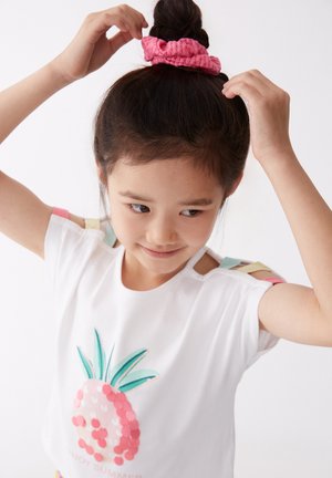 Camisa de manga corta blanca con un diseño de piña rosa. Accentos en los hombros en colores pastel. Niño/a lleva una diadema arrugada rosa en el cabello.